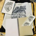 Heart to Hartman logo on a backpack, notebook, and stickers